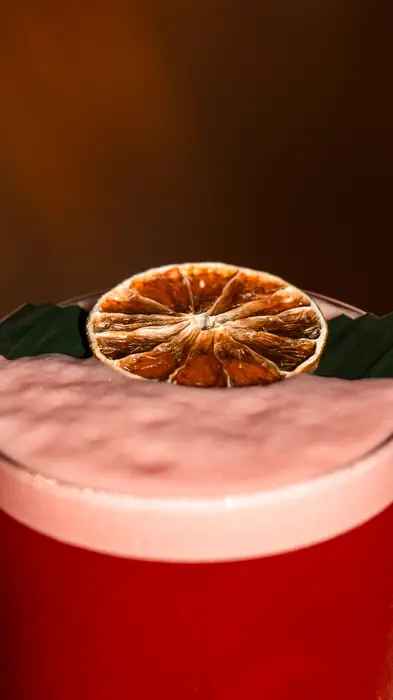 Pink cocktail topped with a dried orange slice